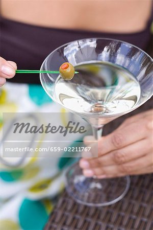 Femme tenant vert olive sur cocktail bâton sur le verre à Martini Femme tenant vert olive sur cocktail bâton sur le verre à Martini