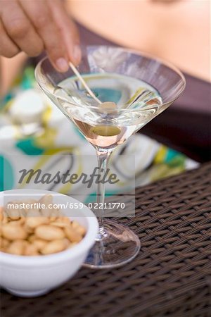 Woman holding green olive on cocktail stick in Martini glass Woman holding green olive on cocktail stick in Martini glass