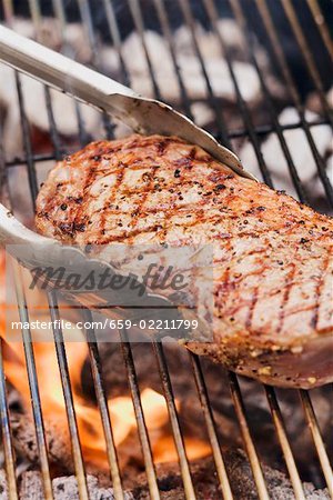 Beef steak on a barbecue with barbecue tongs Beef steak on a barbecue with barbecue tongs