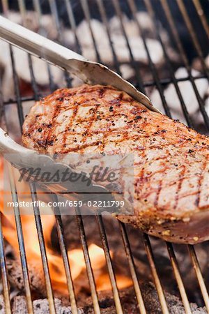 Beef steak on a barbecue with barbecue tongs