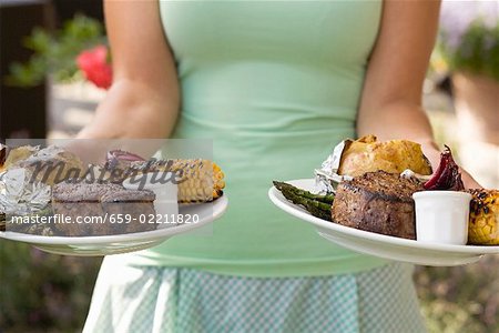 Woman serving two plates of grilled steak & accompaniments Woman serving two plates of grilled steak & accompaniments