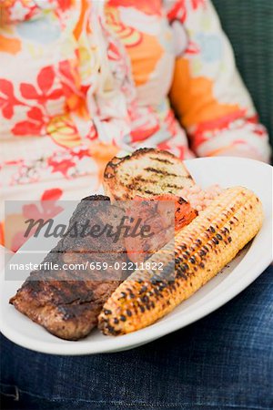 Woman holding a plate of grilled steak and accompaniments