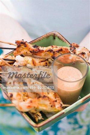 Woman holding grilled satay with dip