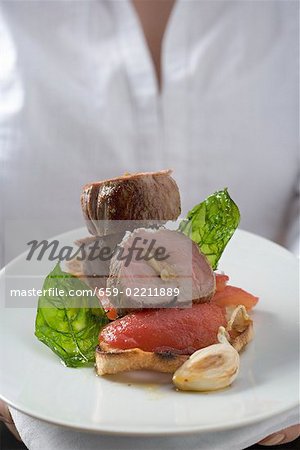 Woman serving pork fillet, tomatoes and basil on toast