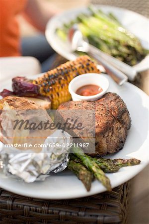 Grilled beef steak with baked potato, corn on the cob, asparagus