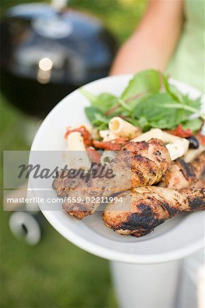 Woman holding plate of grilled chicken legs & pasta salad