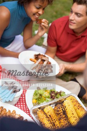 Couple avec côtes levées grillées, maïs en épi, salade, sur l'herbe