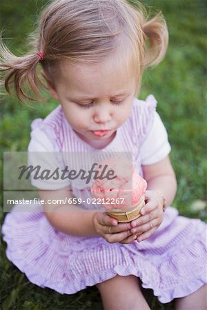 Petite fille assise sur l'herbe, holding de cône de crème glacée à la fraise