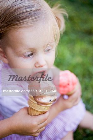 Child's hand offering small girl a lick of ice cream