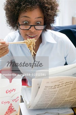 Frau im Büro asiatisches Nudelgericht Essen & lesen Zeitung
