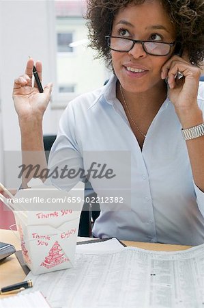 Woman in office with Asian noodle dish, on the phone