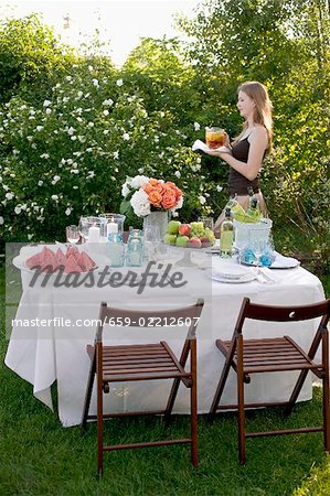 Woman bringing drink to table laid in garden