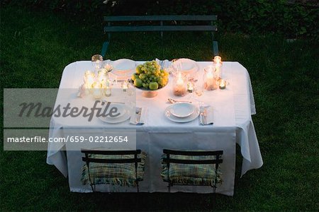Bowl of fruit and windlights on table laid in garden