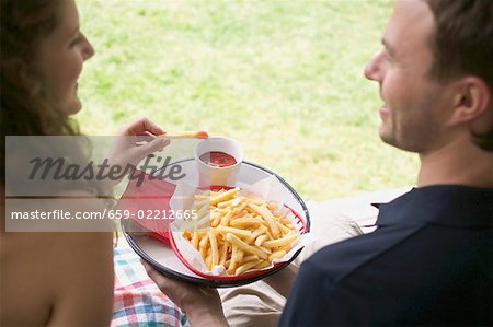 Couple eating chips with ketchup in garden