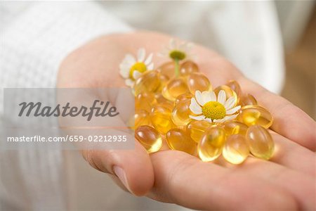 Hand hält Vitamin Kapseln und Kamillenblüten