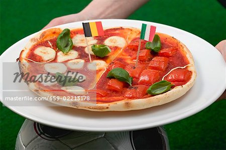Mains tenant la tomate et mozzarella pizza avec drapeaux