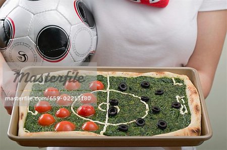 Footballeuse holding pizza épinards avec tomates & olives