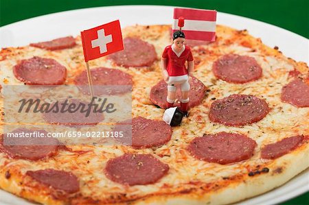 Salami pizza with toy footballer and two flags