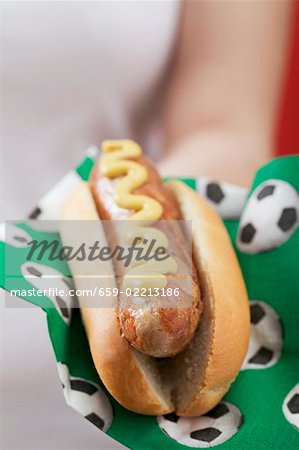 Woman holding hot dog with mustard on napkin with football motifs