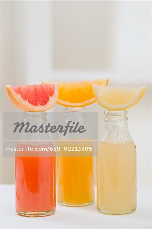 Three fruit juices in bottles with wedges of fresh fruit