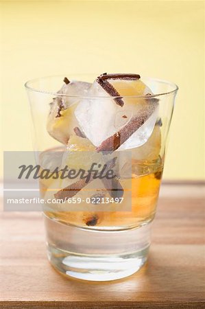 Rum and ice cubes with spices and pieces of fruit in glass