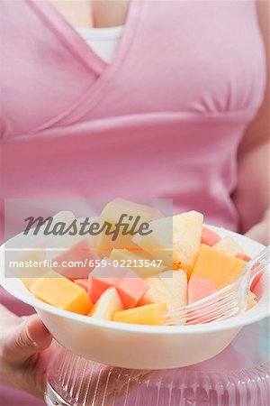 woman holding exotic fruit salad in plastic dish