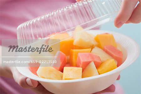 Femme, retirer le couvercle en plastique plat de salade de fruits exotiques