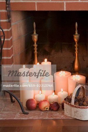 Kerzen, Granatäpfel und Zapfen vor Kamin