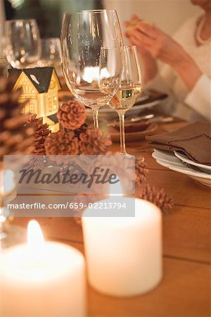 Wine glasses & candles on Christmas table, woman in background