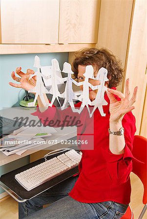 Woman holding row of paper dolls in home office