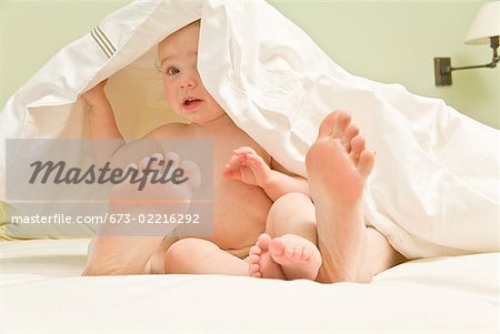 Bébé et les pieds de la mère sous couverture dans le lit