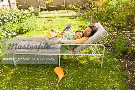 Mother and son sleeping on lounge chair in backyard garden