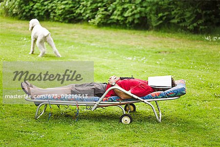 Homme avec le magazine sur le visage relaxant dans une chaise longue au jardin