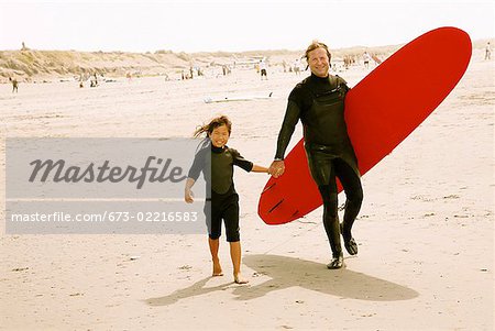 Père et fille transportant des planches de surf sur la plage