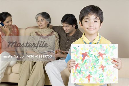 Portrait of a boy holding a painting and family sitting behind him