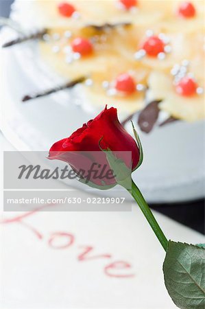 Close-up of a red rose near a cake with a greeting card