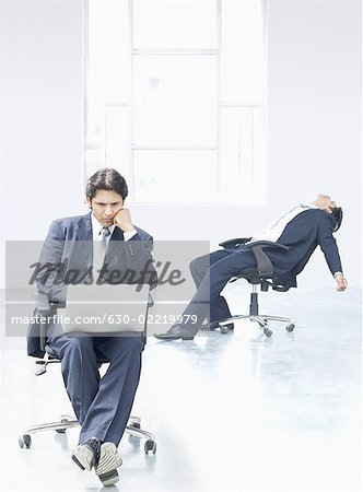 Kaufmann mit einem Laptop mit einem anderen kaufmann liegend auf einem Stuhl in einem Büro