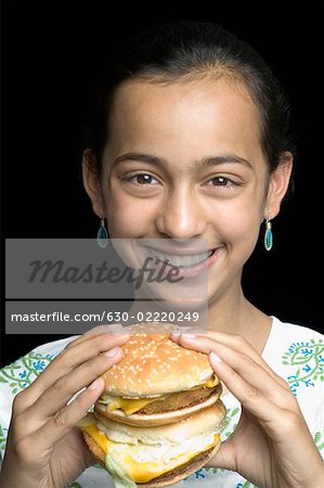 Portrait d'une jeune fille tenant un burger et souriant