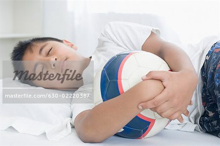 Junge schlafen auf dem Bett und hält einen Fußball