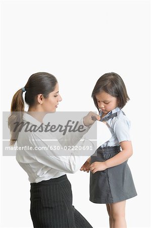 Profil de côté d'une jeune femme aide sa fille à porter l'uniforme scolaire