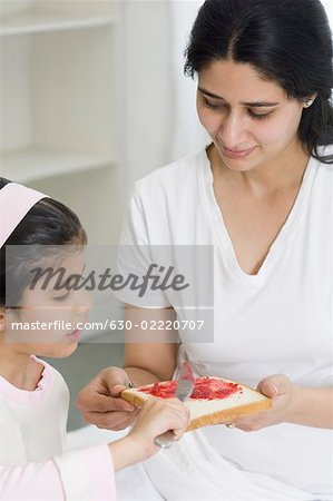 Close-up of a girl spreading jam on a bread with her mother