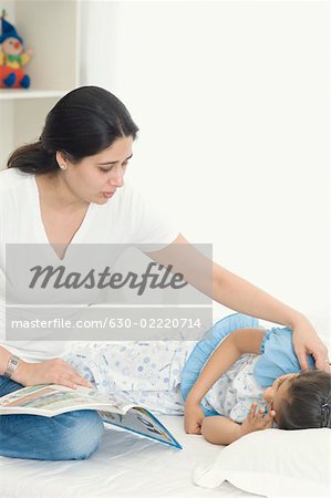 Mid femme adulte assis à côté de sa fille de dormir sur le lit
