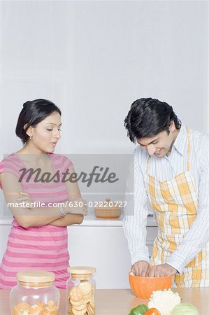 Mid adult woman looking at her husband preparing food