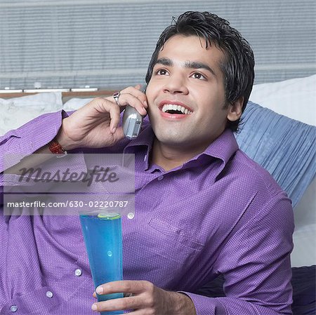 Junger Mann hält ein Glas blau Cucacao und sprechen auf ein schnurloses Telefon