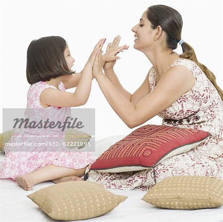 Side profile of a young woman playing high-five with her daughter on the bed and smiling