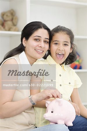 Portrait of a mid adult woman putting a coin in a piggy bank and smiling with her daughter