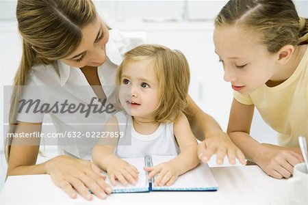 Woman sitting together with two daughters, looking at open notebook on table