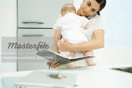 Woman holding baby, using cell phone and looking at agenda