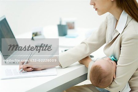 Young professional woman in office, holding sleeping infant, signing document