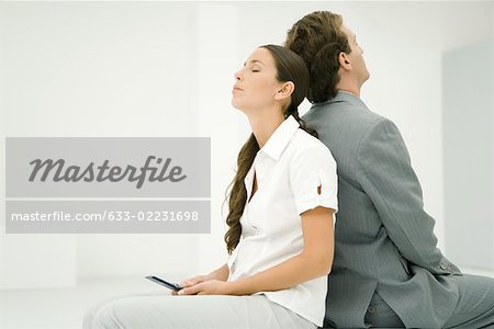 Two professionals sitting back to back, eyes closed, woman holding cell phone